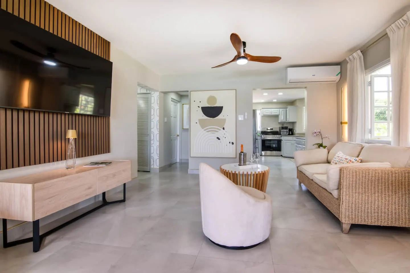 Living room with large TV, air conditioning and kitchen alongside.